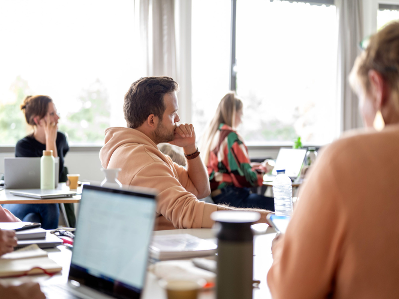Mannelijke student in klas die kijkt naar de docent met andere studenten op de achtergrond
